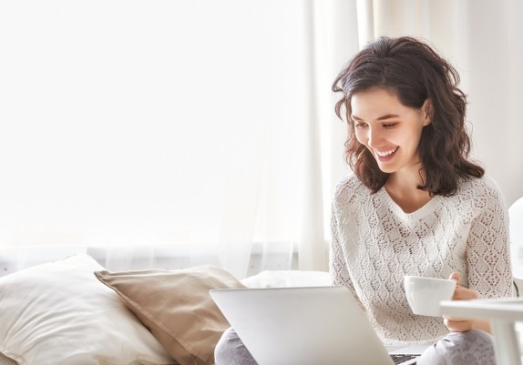 Junge Frau mit Kaffee am Laptop auf der Couch